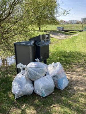 Mehrere gefüllte weiße Müllsäcke, angelehnt an einen Mülleimer im Park