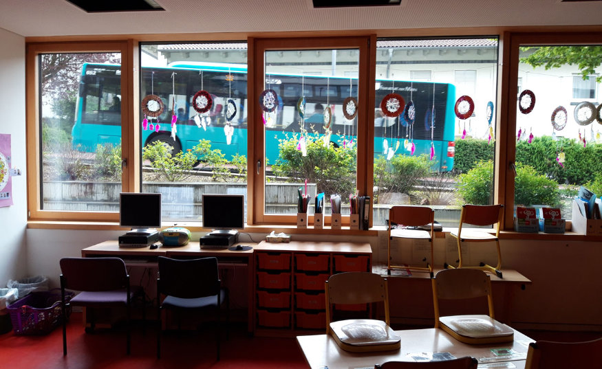 Blick auf einen wartenden Bus aus einem Klassenzimmer heraus.